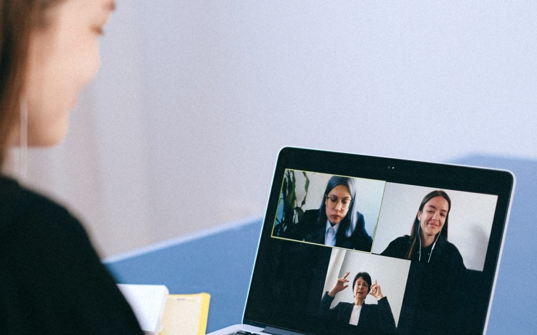 Woman seen in an over the shoulder shot during a virtual meeting on her laptop with three others pictured on screen