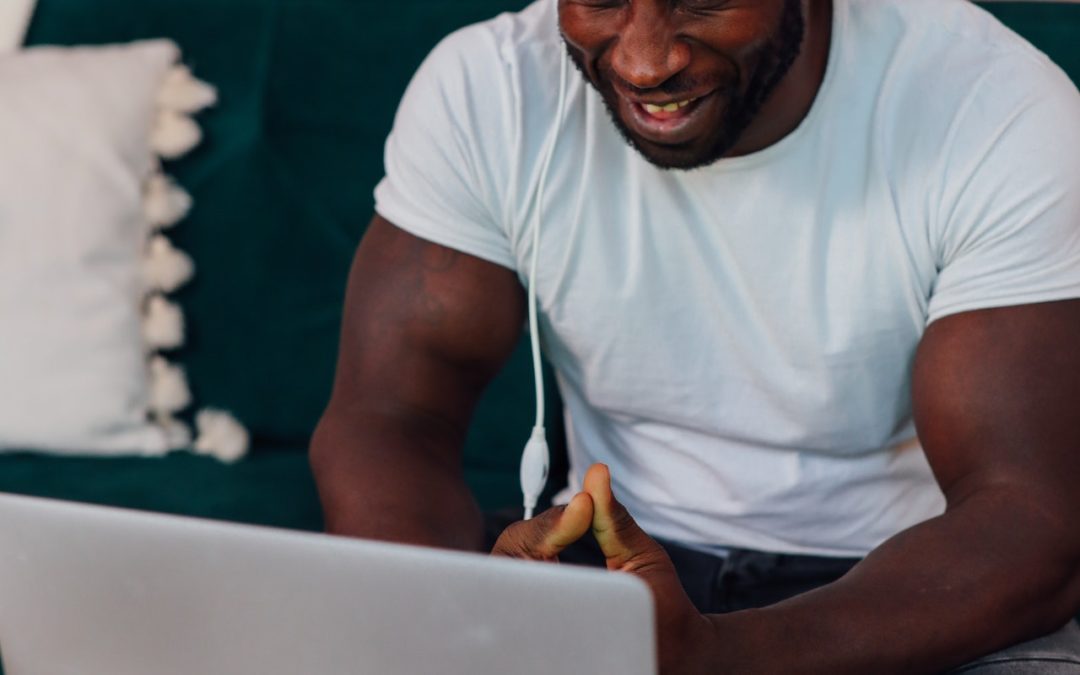 Man sits on couch with over the ear headphones on while looking at an Apple laptop on lowered table in front of him