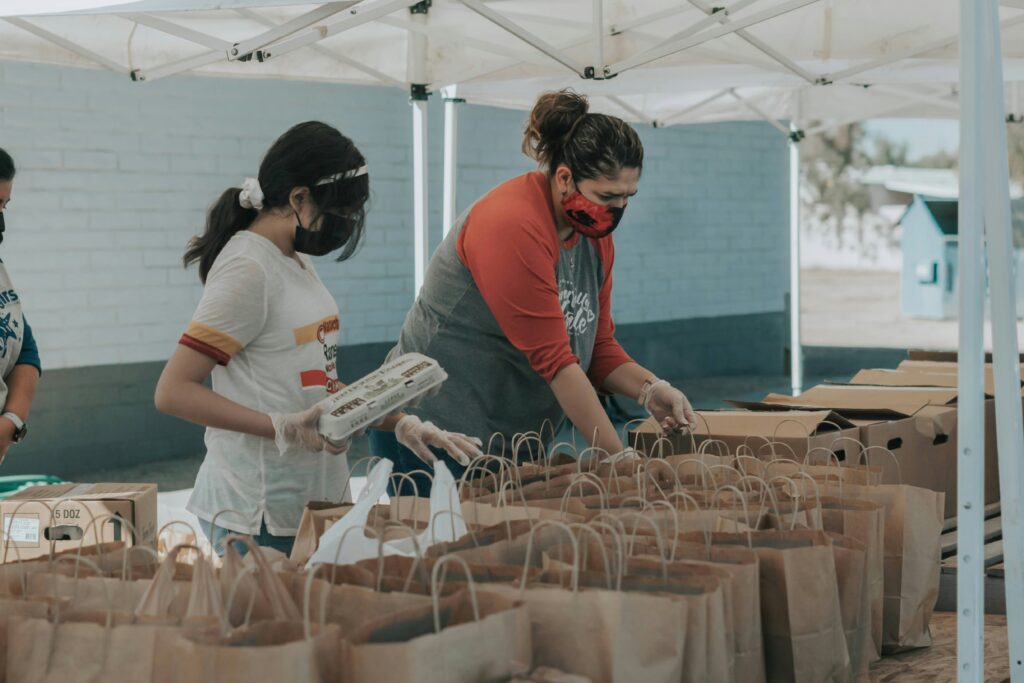 A girl and woman sorting out items into brown paper bags at a food drive