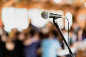 Shot of a microphone with seated people and twinkling lights out of focus in the background